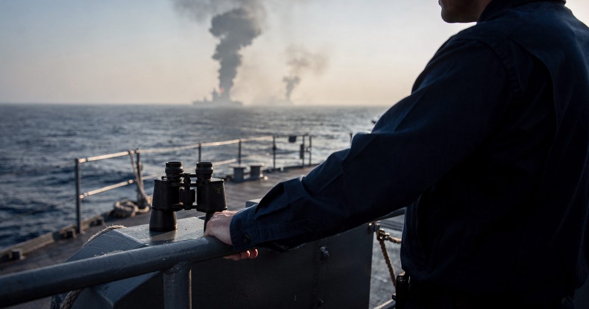 Late afternoon sunlight on the steel deck of a US Navy destroyer in open water, two sailors framed from the shoulders down leaning on the rail as they watch a.